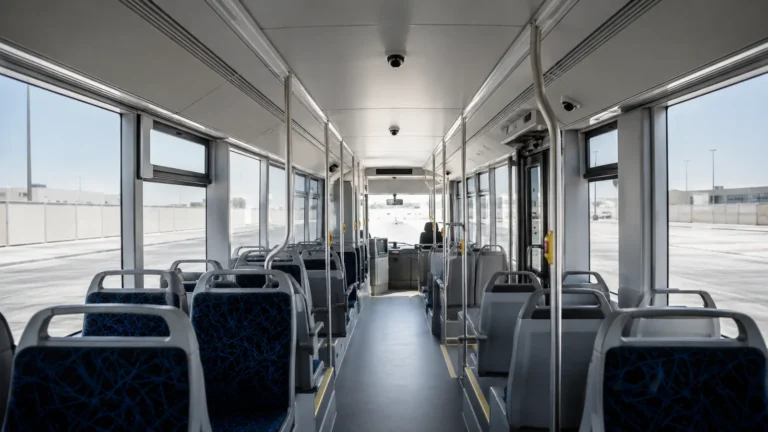 Interior of a city bus looking down the aisle towards the doors, with a dome camera on the ceiling